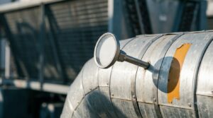 Coolant Supply Temperature Buys Free Cooling Hours at a Cost - Data Center Technology Lab Stainless thermowell and dial thermometer on an insulated facility water pipe under hard directional light